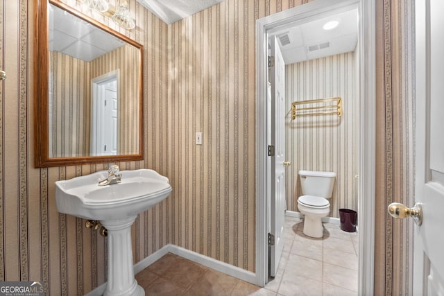 half bathroom featuring wallpapered walls, toilet, tile patterned flooring, and baseboards