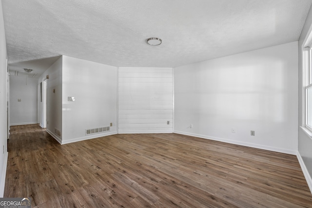 unfurnished room with baseboards, visible vents, wood finished floors, and a textured ceiling