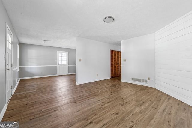 empty room featuring wood walls, a textured ceiling, visible vents, and wood finished floors