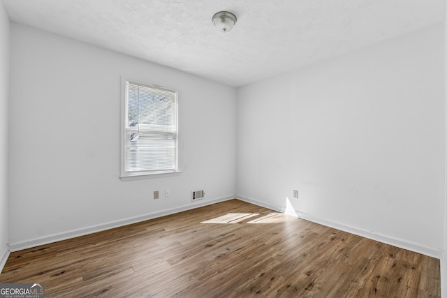 unfurnished room featuring wood finished floors, a textured ceiling, baseboards, and visible vents