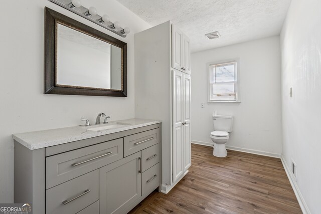 bathroom featuring a textured ceiling, visible vents, toilet, wood finished floors, and vanity