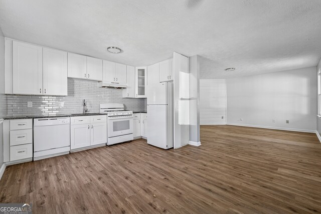 kitchen with white appliances, dark countertops, dark wood finished floors, under cabinet range hood, and backsplash