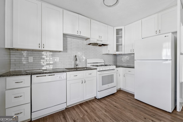 kitchen with a sink, dark wood-style flooring, under cabinet range hood, white appliances, and dark stone counters