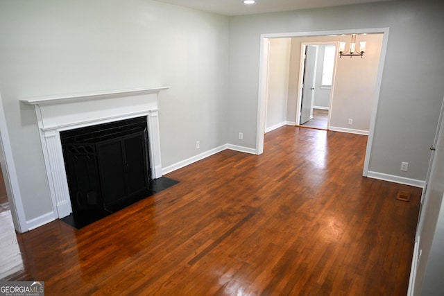 unfurnished living room with a fireplace with flush hearth, dark wood-style flooring, baseboards, and a chandelier