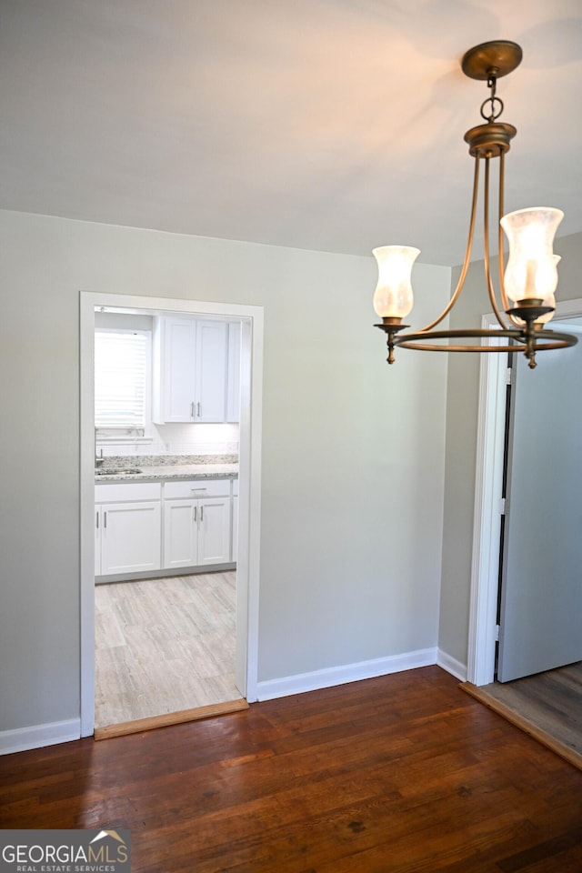 interior space with baseboards, wood finished floors, a sink, and an inviting chandelier