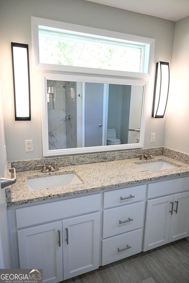 bathroom featuring double vanity, a sink, toilet, and a tile shower