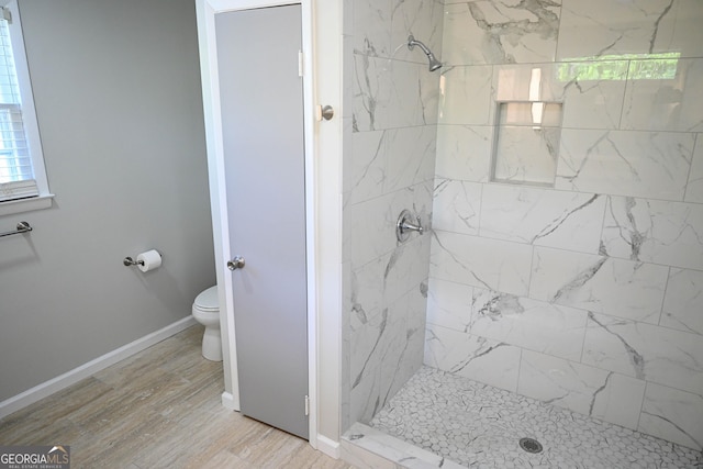 bathroom featuring baseboards, wood finished floors, toilet, and a shower stall