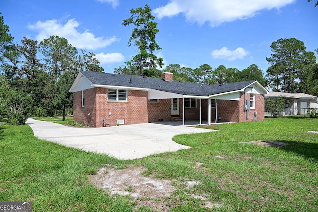 back of property featuring driveway, a chimney, brick siding, a lawn, and crawl space