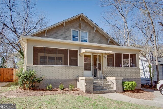 bungalow-style home featuring a sunroom, fence, and brick siding