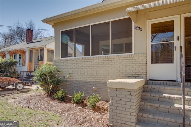 view of property exterior featuring brick siding, a sunroom, and a chimney