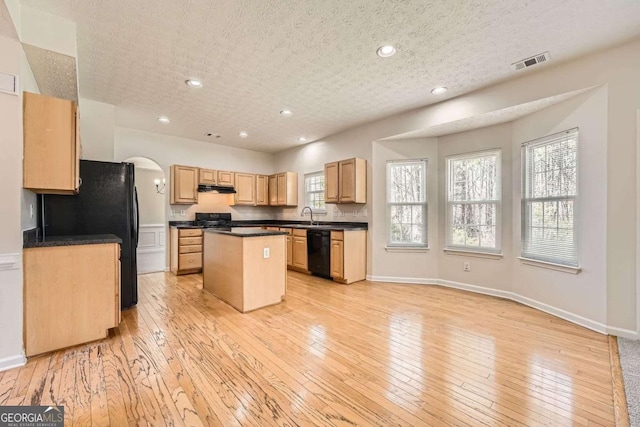 4157 Medlock Woods Dr, Snellville, GA 30039 - kitchen with light wood finished floors, a center island, under cabinet range hood, visible vents, and black appliances