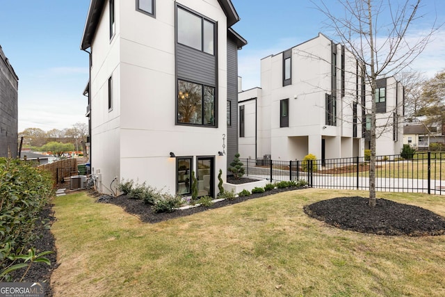 view of side of property featuring stucco siding, fence, central AC unit, and a yard