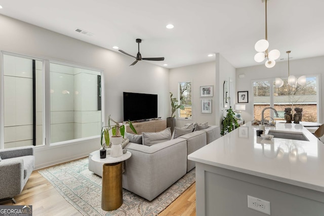 living area with light wood-style floors, visible vents, recessed lighting, and ceiling fan with notable chandelier