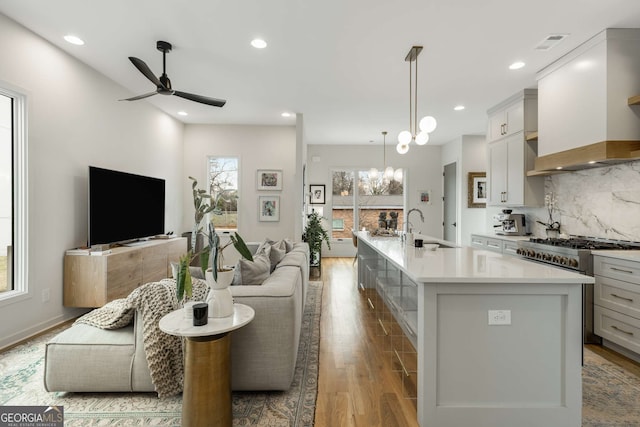 kitchen with light countertops, wood finished floors, a sink, custom range hood, and open floor plan