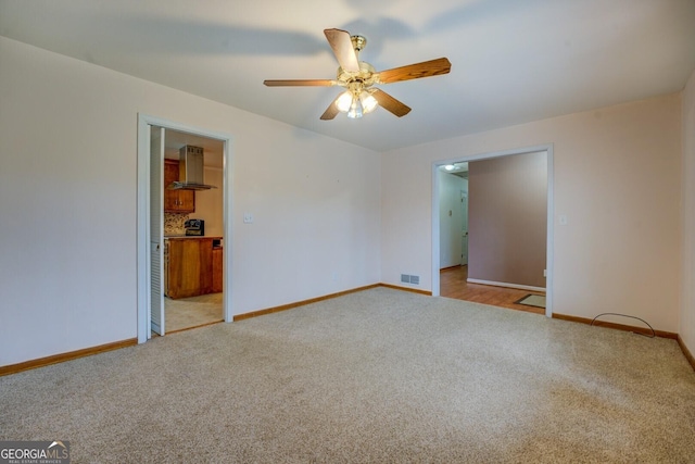 carpeted spare room with baseboards, visible vents, and ceiling fan