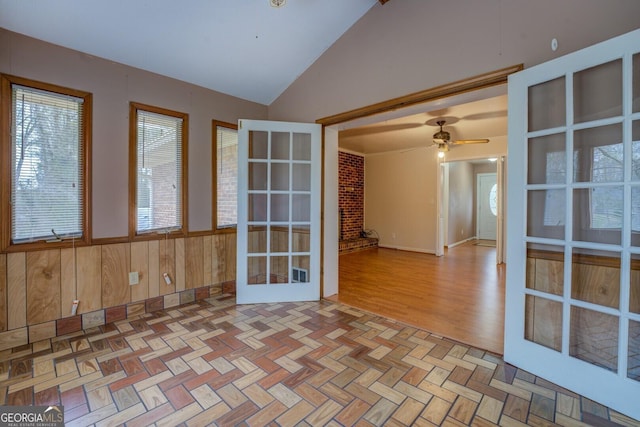unfurnished room with a wainscoted wall, wood walls, ceiling fan, parquet floors, and french doors