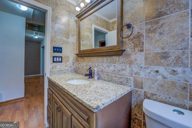 half bath with tile walls, crown molding, toilet, wood finished floors, and vanity