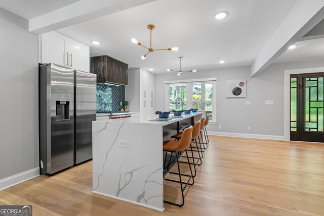 kitchen featuring white cabinets, stainless steel fridge with ice dispenser, light wood-style flooring, and baseboards