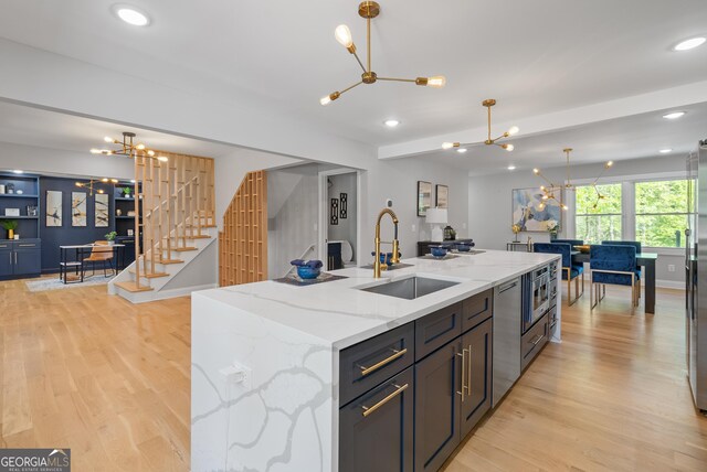 kitchen with stainless steel appliances, light wood-style flooring, a sink, and an inviting chandelier