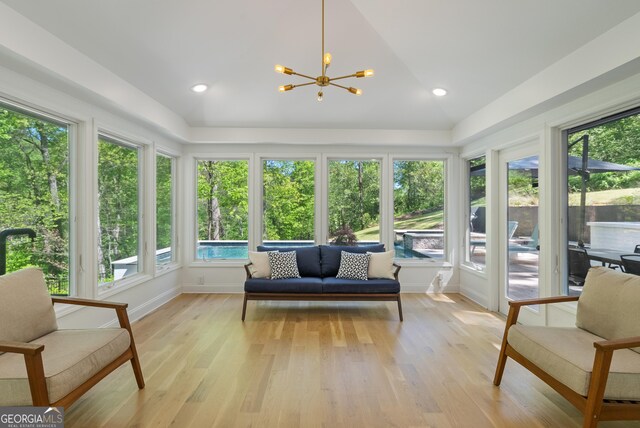 sunroom featuring vaulted ceiling, wood finished floors, baseboards, and an inviting chandelier