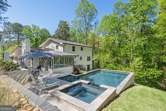 rear view of property with a chimney, a patio area, a lawn, a pool with connected hot tub, and a sunroom