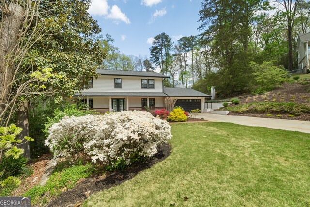 traditional-style home with concrete driveway, a front lawn, a garage, and french doors