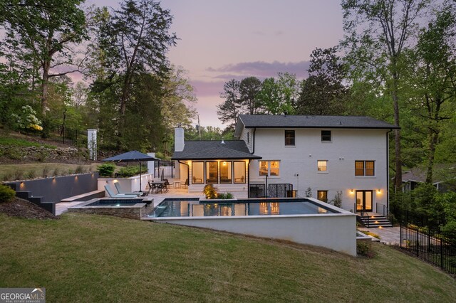 rear view of property with a lawn, a chimney, a fenced in pool, and an in ground hot tub