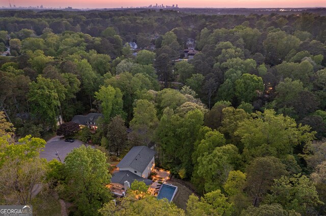aerial view at dusk featuring a wooded view