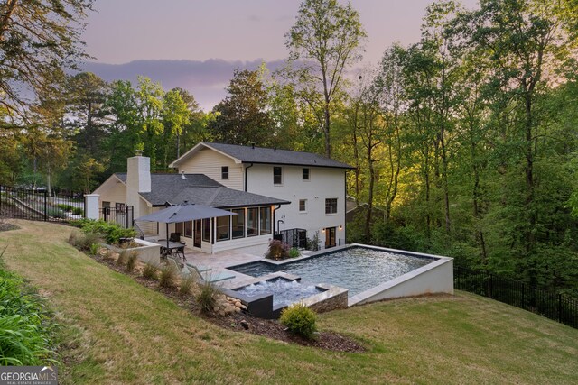 back of property at dusk with a fenced in pool, a chimney, a yard, a patio area, and a sunroom
