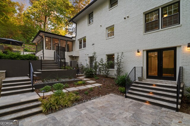 back of property featuring french doors, central air condition unit, brick siding, stairway, and a sunroom