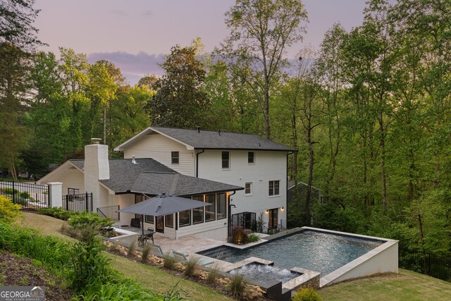 back of house with a fenced in pool, roof with shingles, fence, a sunroom, and a patio
