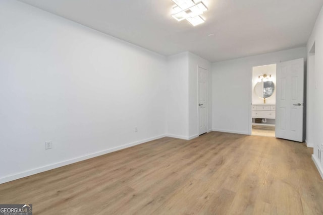 unfurnished bedroom with baseboards, ensuite bath, and light wood-style flooring
