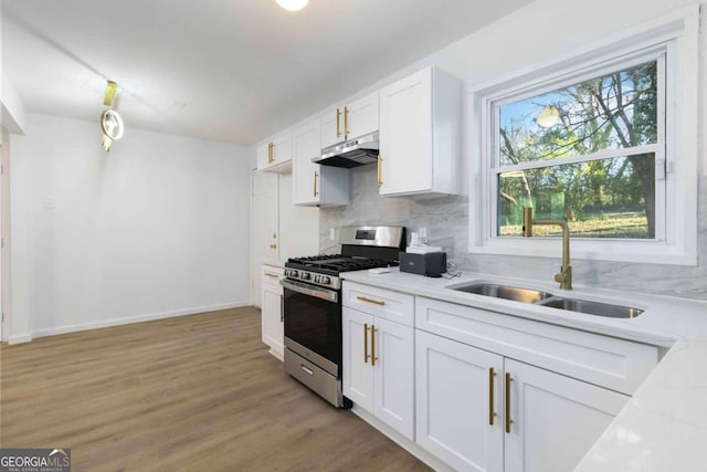 kitchen with stainless steel range with gas cooktop, under cabinet range hood, backsplash, a sink, and white cabinets