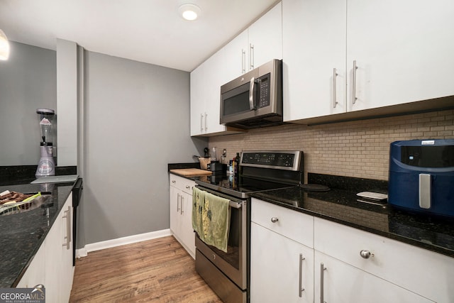 3501 Roswell Rd NE Unit 211, Atlanta, GA 30305 - kitchen with appliances with stainless steel finishes, backsplash, white cabinetry, light wood finished floors, and dark stone countertops
