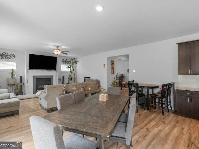 dining room with ceiling fan, a glass covered fireplace, and light wood-style floors