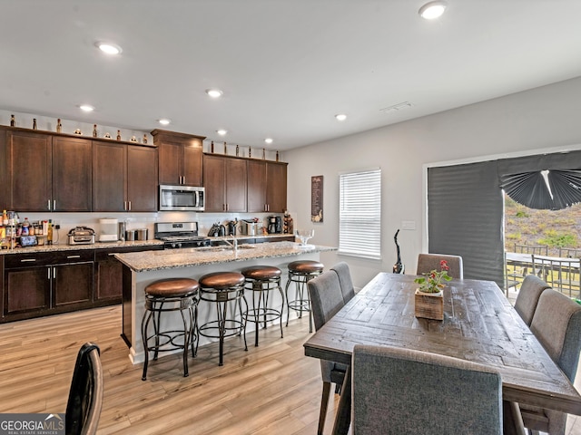 kitchen featuring a kitchen breakfast bar, an island with sink, stainless steel appliances, and light wood-style floors