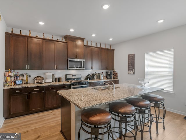 kitchen featuring a sink, stainless steel appliances, light wood-style floors, and a breakfast bar