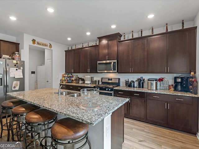 kitchen featuring light wood-style flooring, a kitchen bar, recessed lighting, appliances with stainless steel finishes, and a sink