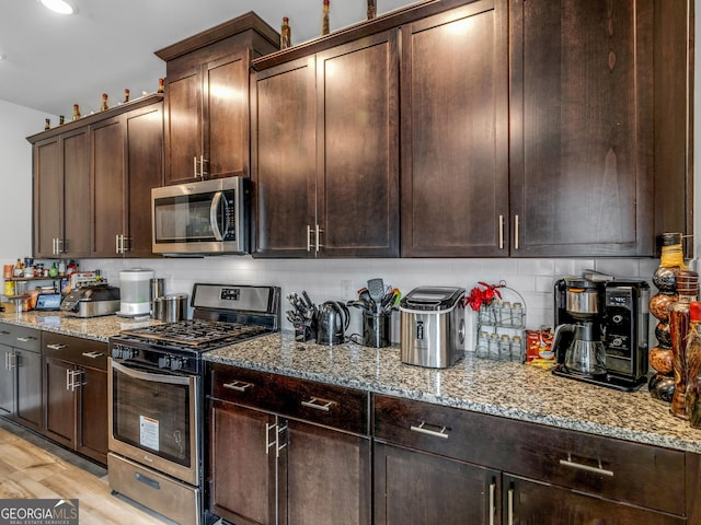 kitchen with light wood finished floors, stainless steel appliances, dark brown cabinetry, light stone counters, and backsplash