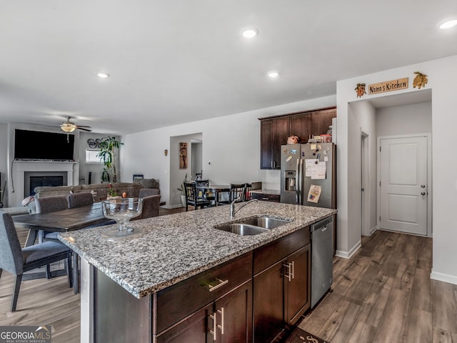 kitchen featuring stainless steel appliances, a ceiling fan, a sink, light stone counters, and dark wood-style floors