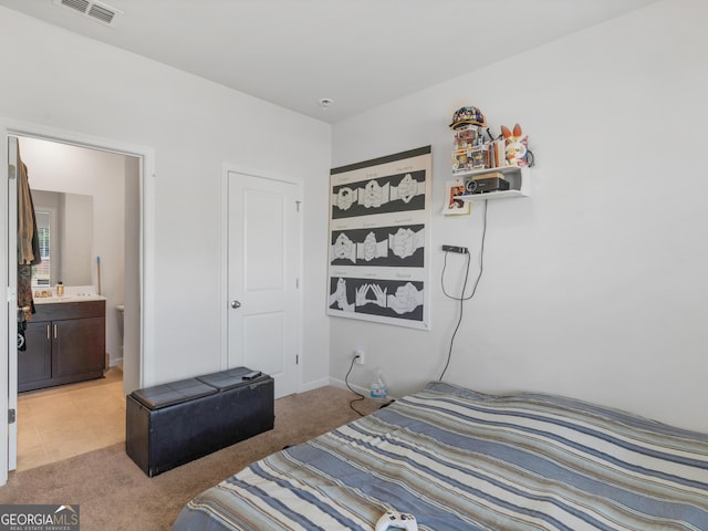 bedroom with light carpet, visible vents, and ensuite bath