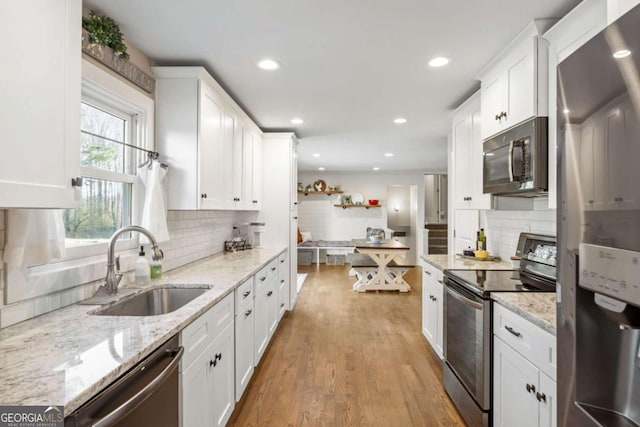 kitchen with stainless steel appliances, decorative backsplash, a sink, light wood-style floors, and white cabinets
