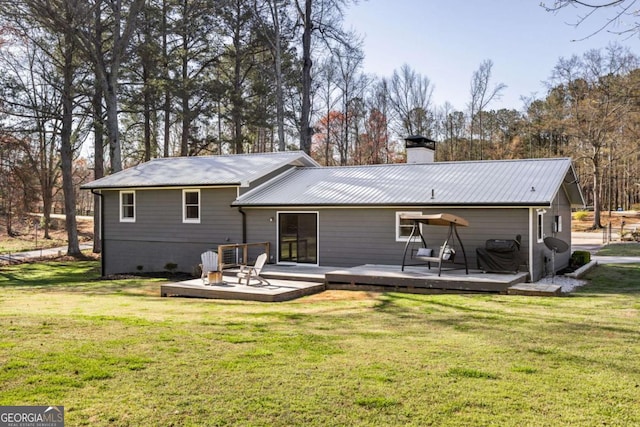 rear view of house featuring a chimney, a lawn, and a wooden deck