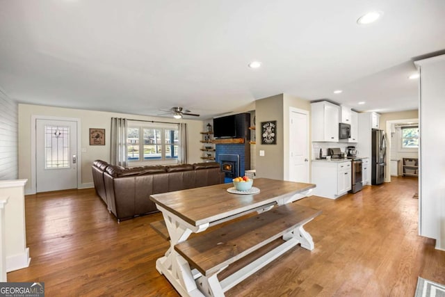 living room featuring a warm lit fireplace, light wood-type flooring, ceiling fan, and recessed lighting