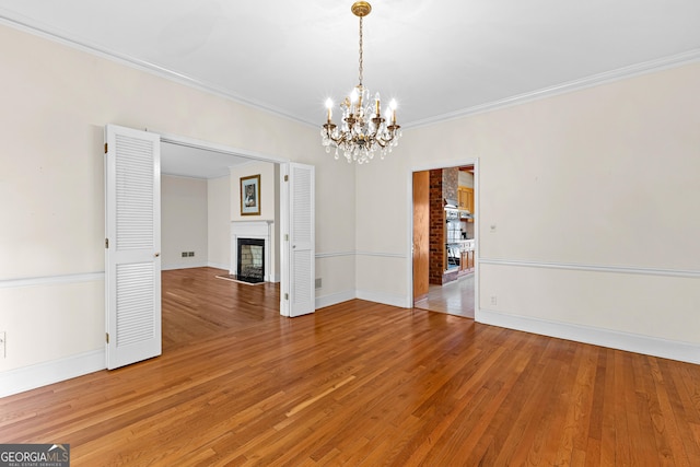 9095 Cedar Grove Rd, Fairburn, GA 30213 - spare room with crown molding, a fireplace with flush hearth, baseboards, a chandelier, and light wood-style floors