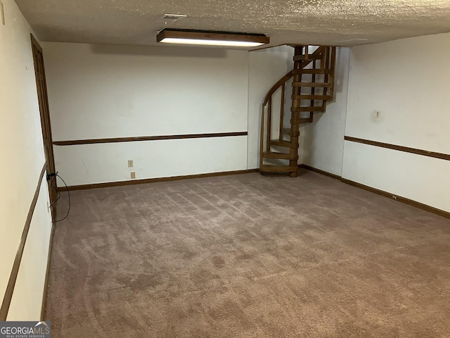 finished below grade area featuring carpet floors, a textured ceiling, baseboards, and stairway