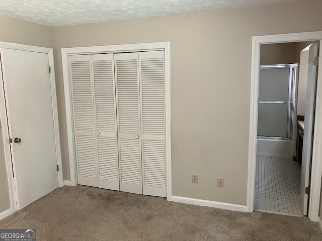 unfurnished bedroom featuring ensuite bath, carpet floors, a textured ceiling, baseboards, and a closet