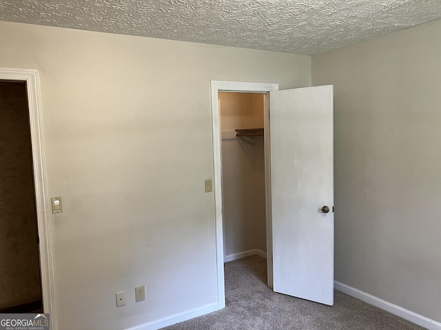 unfurnished bedroom featuring a walk in closet, a textured ceiling, carpet, baseboards, and a closet