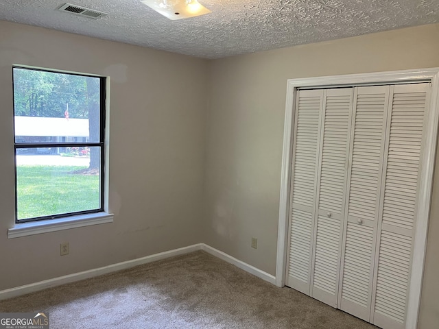 unfurnished bedroom with visible vents, a closet, baseboards, a textured ceiling, and carpet flooring