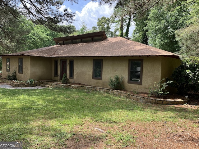 view of front of property with roof with shingles, stucco siding, and a front yard